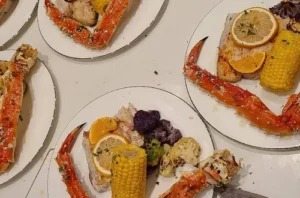 Alaskan king crab legs served with lemon, corn, fish, and assorted vegetables on dinner plates