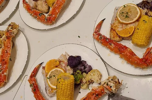 Alaskan king crab legs served with lemon, corn, fish, and assorted vegetables on dinner plates